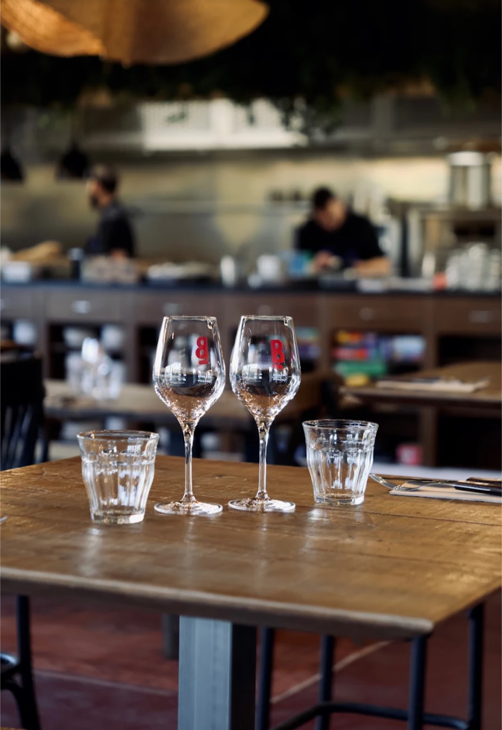 Deux verres à vin marqués du B rouge du Bal, cuisine ouverte en arrière-plan