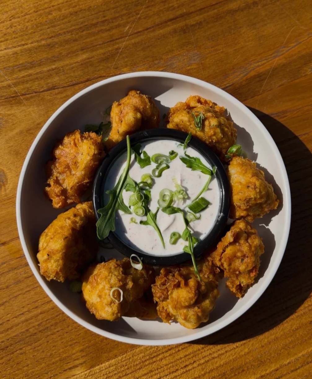 Bol de beignets dorés servis avec une sauce blanche et de la roquette