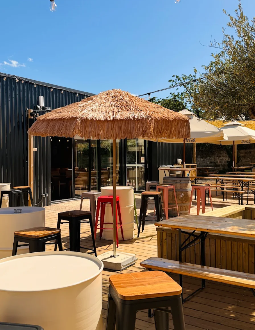 La terrasse en bois du Bal, parasol paillote, tabourets colorés et guirlandes